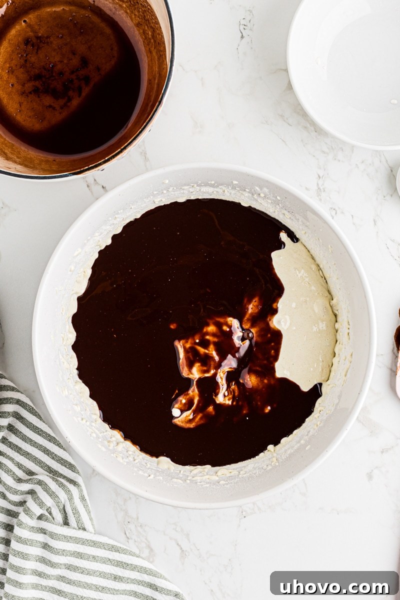 Overhead view of melted chocolate mixture added to brownie batter ingredients in bowl.
