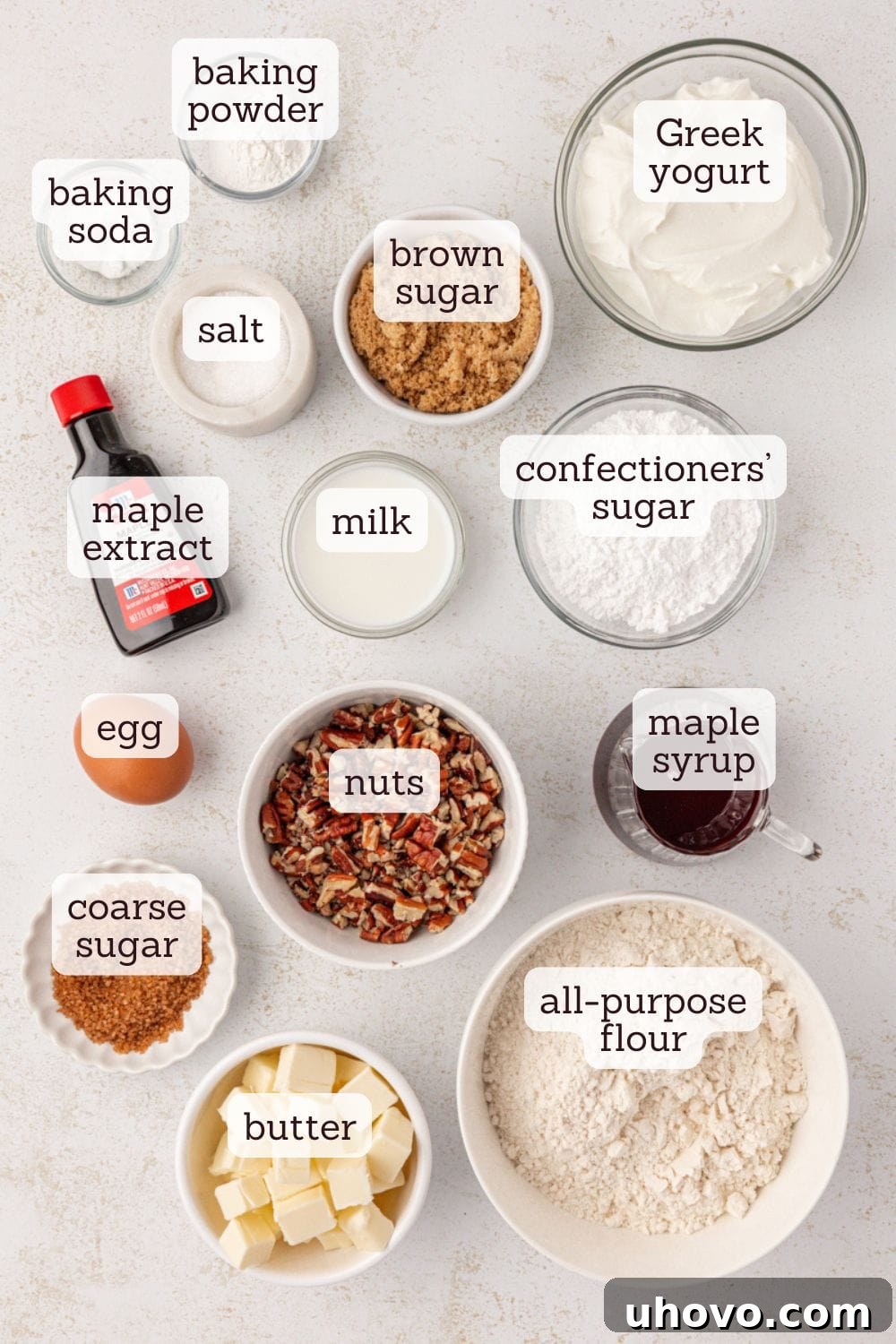An overhead view captures the essential ingredients for maple pecan scones laid out on a clean surface: bags of flour and brown sugar, baking powder, baking soda, salt, cold butter cubes, chopped pecans, a bowl of Greek yogurt, maple syrup, and an egg yolk.