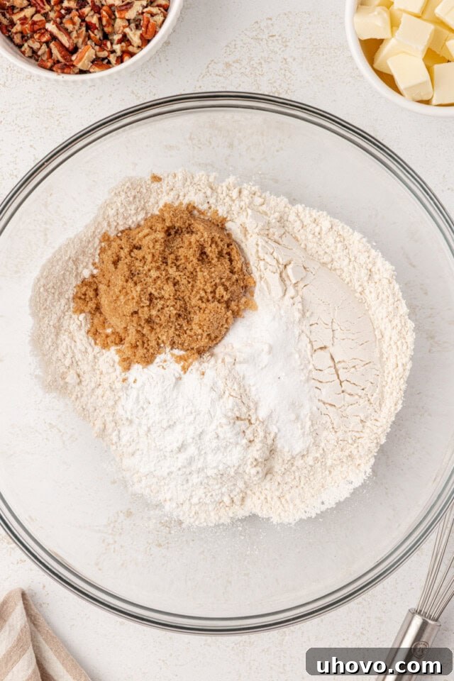 Overhead view of all-purpose flour, brown sugar, baking powder, baking soda, and salt mixed in a glass bowl, ready for butter.