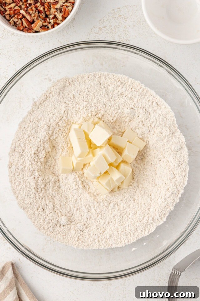 Cold, cubed unsalted butter being added to the bowl of dry ingredients for scones, showing the preparation for cutting in the butter.