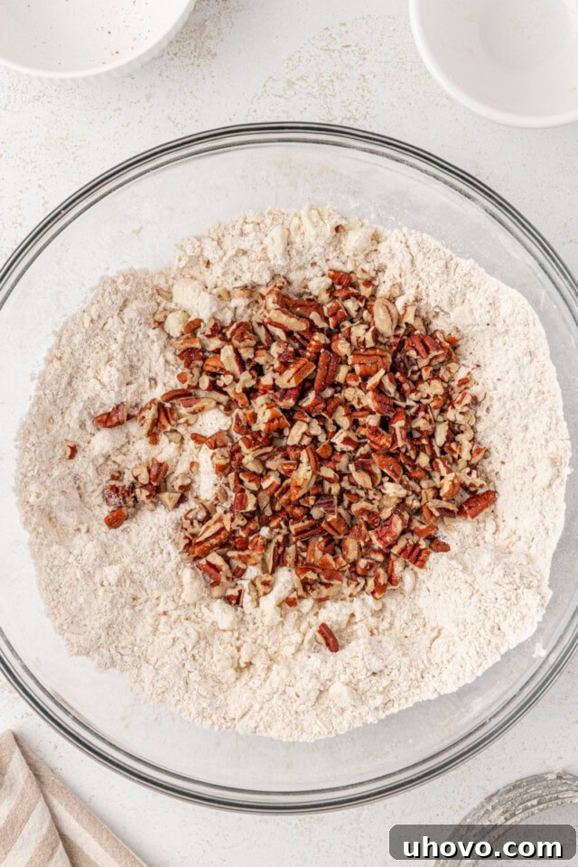 Toasted chopped pecans sprinkled into the scone mixture of flour and butter crumbs, ready to be incorporated.