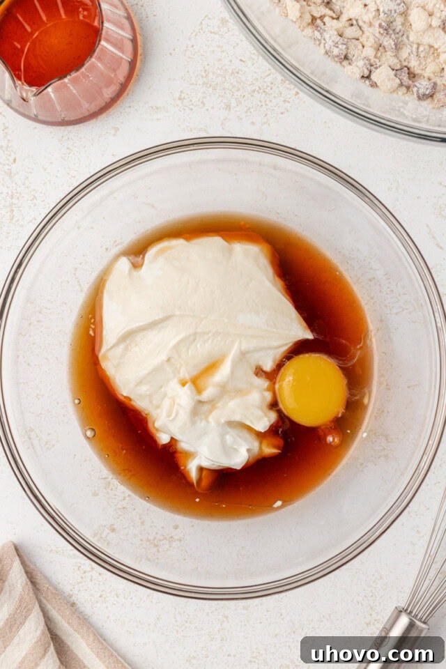 A glass bowl holds a mixture of Greek yogurt, an egg yolk, maple syrup, and maple extract, showcasing the combined wet ingredients for the scones.