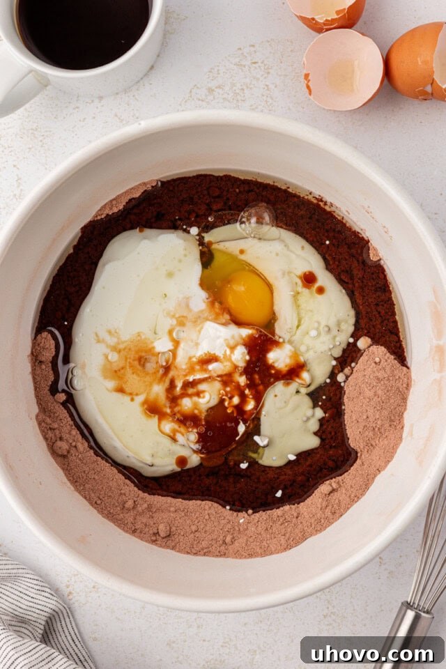 An overhead shot illustrating the process of adding the wet ingredients—eggs, vegetable oil, vanilla extract, and buttermilk—to the dry mixture for the chocolate cake batter.