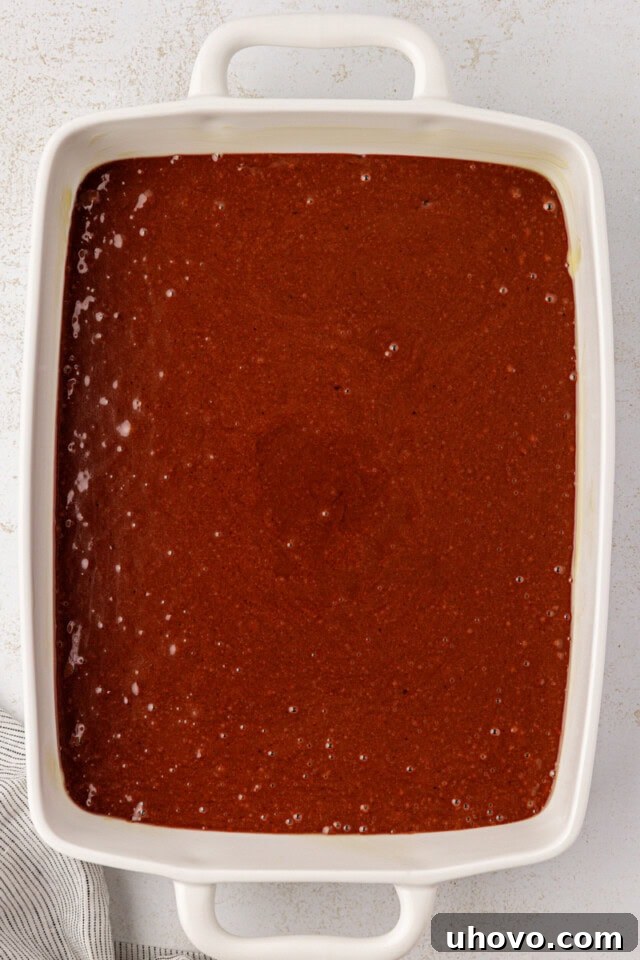 An overhead shot of the smooth chocolate cake batter neatly poured into a white rectangular baking pan, prepped and ready to be placed into the oven for baking.