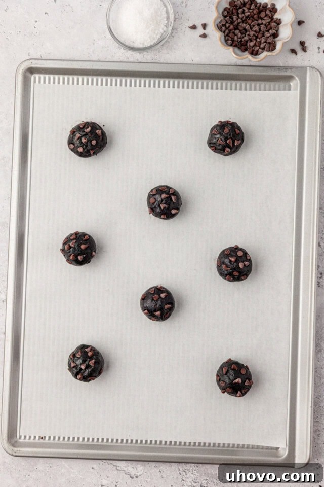 overhead view of black cocoa cookie dough scooped onto a lined baking sheet, ready to go into the oven