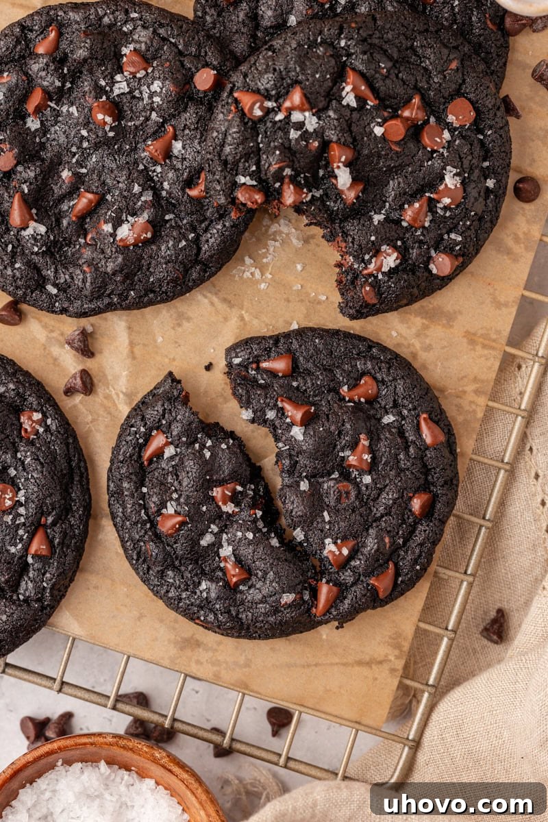 a black cocoa cookie cut in half on parchment paper with more cookies surrounding