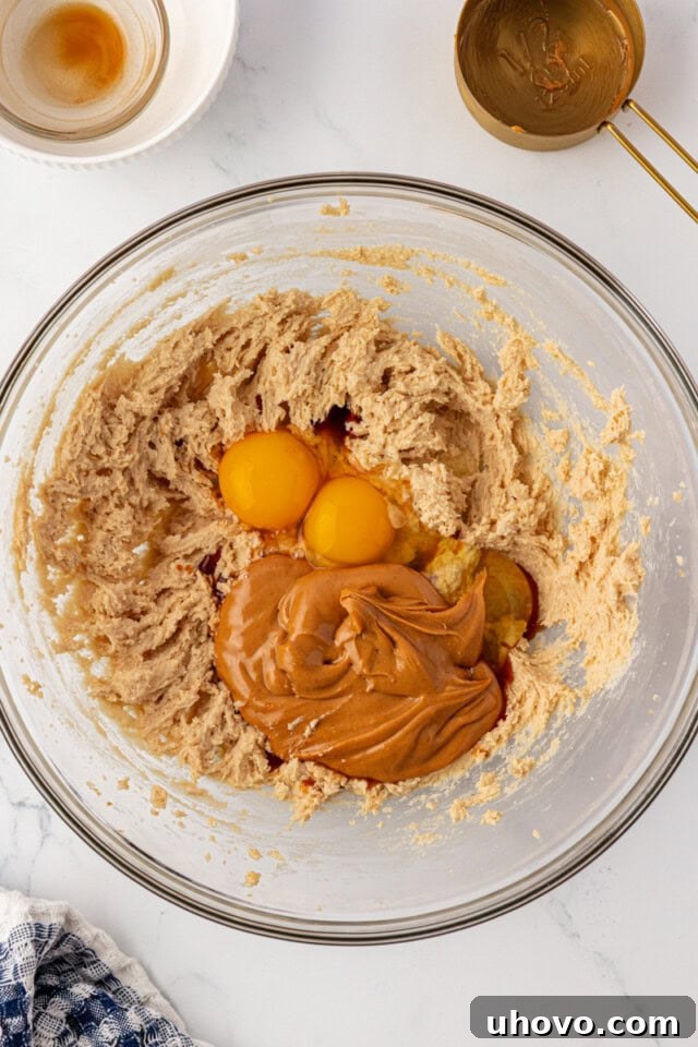 overhead view of peanut butter, eggs, and vanilla added to creamed butter and sugars in a glass mixing bowl