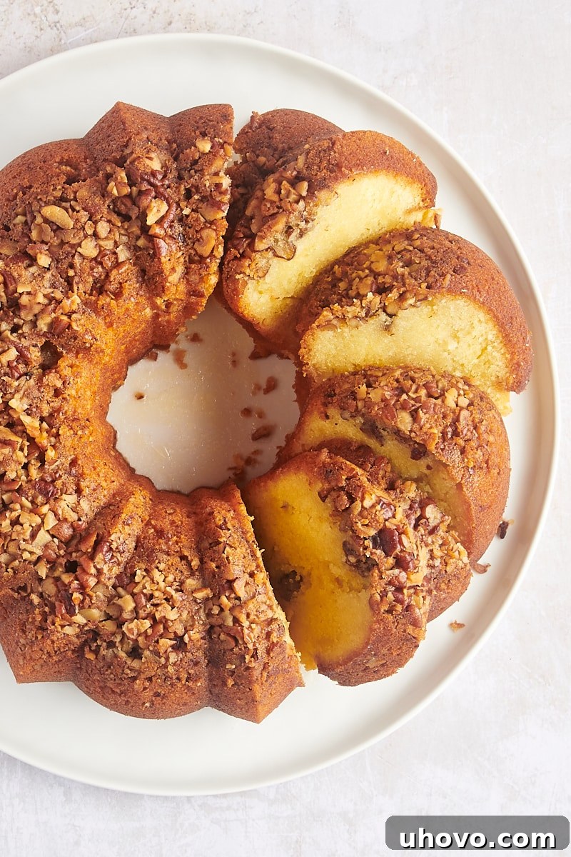 Overhead view of partially cut rum cake on platter, showing its moist interior and pecan topping.