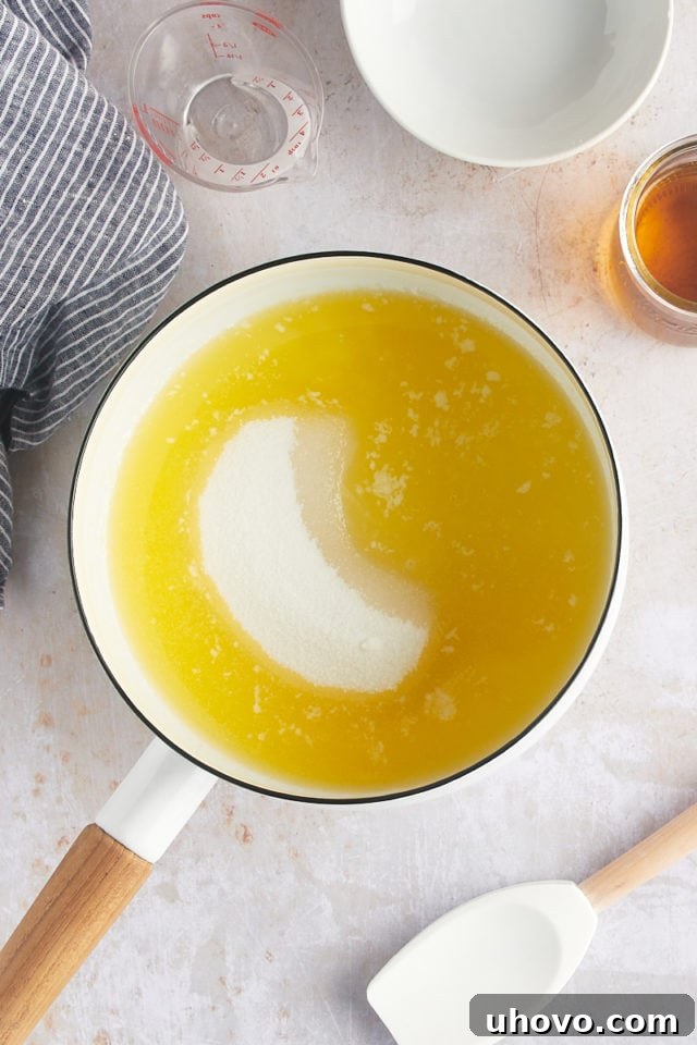 Overhead view of granulated sugar being stirred into the simmering butter and water mixture in a saucepan to create the glaze.