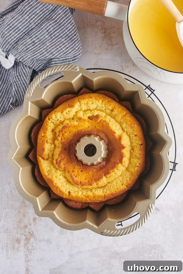 Overhead view of the rum cake in the Bundt pan, resting on a wire rack, with the first half of the warm rum glaze poured over it and soaking in.
