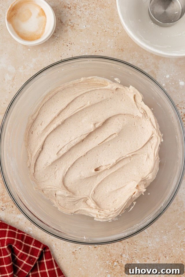 Overhead view of a glass mixing bowl filled with light, fluffy spiced cream cheese frosting, perfectly whipped and ready for piping.