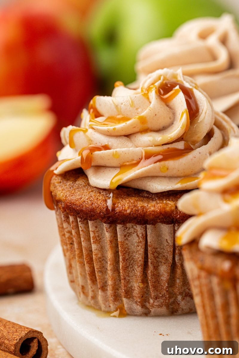 Close-up shot of a single perfectly frosted apple cupcake, elegantly placed on a marble tray and surrounded by more cupcakes and fresh apples, highlighting its tempting appeal.