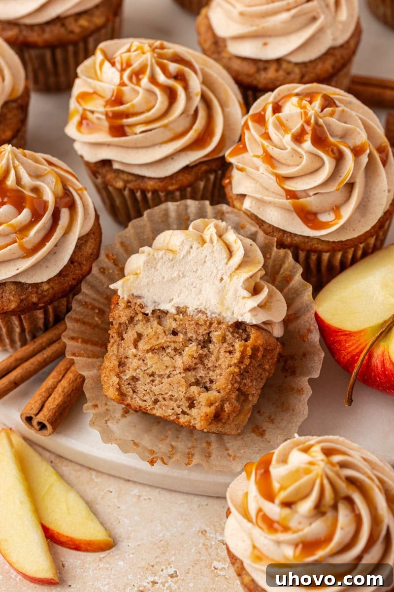 A perfectly baked apple cupcake, halved to reveal its moist, apple-studded interior, beautifully arranged alongside several other whole apple cupcakes on a serving tray.