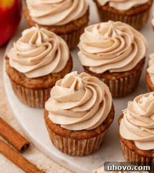Beautiful apple cupcakes topped with spiced cream cheese frosting and a hint of caramel, presented on a marble serving plate.