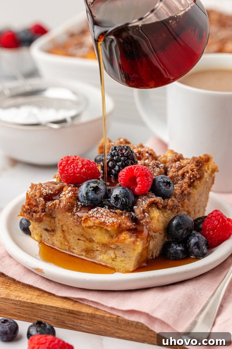 a slice of baked French toast topped with fresh berries with maple syrup being drizzled over it