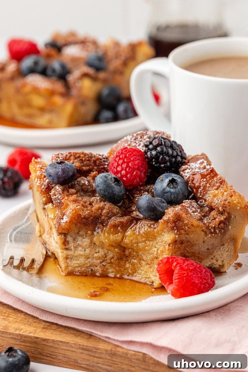 a slice of baked French toast topped with maple syrup and fresh berries on a white plate