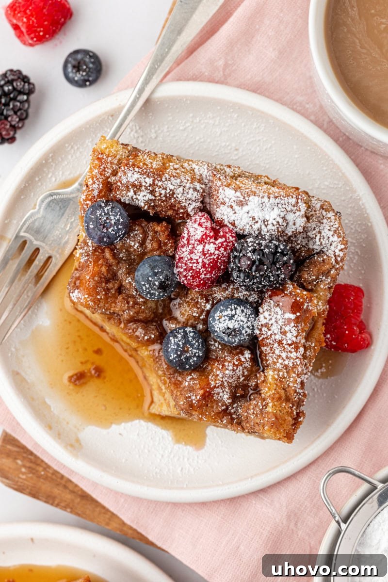 overhead view of a slice of baked French toast on a white plate with a bite missing