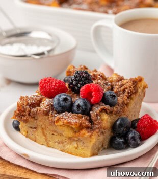 a slice of baked French toast on a white plate with the remaining French toast and a cup of coffee in the background
