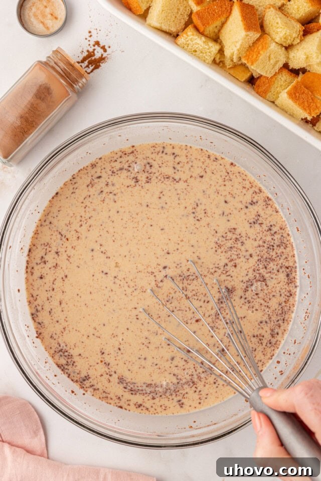 overhead view of eggs, milk, cream, sugar, vanilla, and spices whisked together in a glass bowl