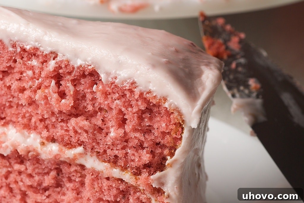A close-up shot of the stunning pink strawberry cake, showcasing its perfectly even layers and smooth, creamy strawberry cream cheese frosting.