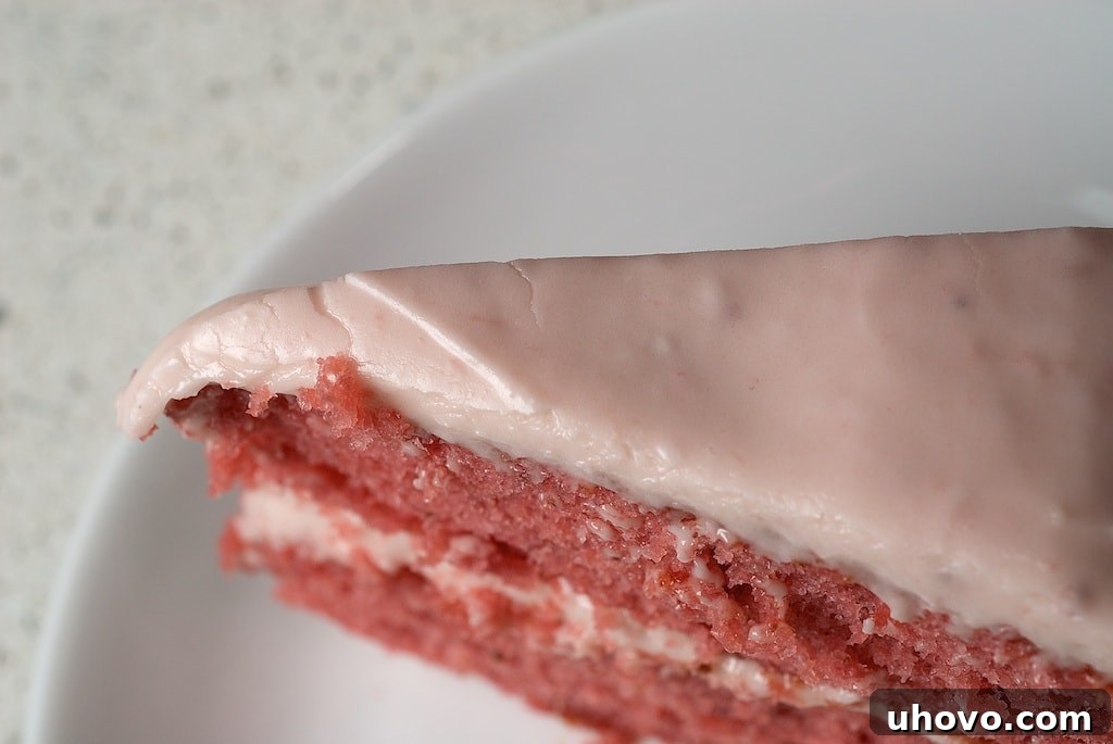 A detailed close-up of the top of the strawberry cake, showcasing the smooth, luscious strawberry cream cheese frosting and a single, perfectly placed fresh strawberry garnish.