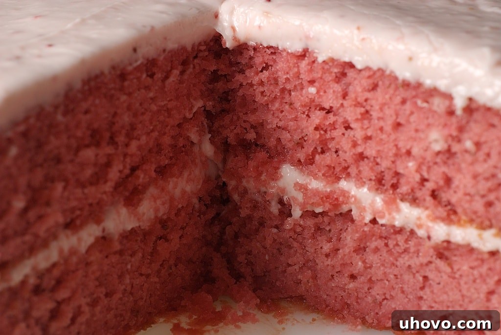 A cross-section view of the strawberry cake, revealing its perfectly pink, moist layers separated by generous dollops of creamy strawberry frosting.