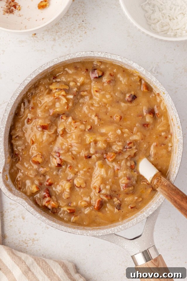 Overhead view of the rich coconut-pecan frosting cooling and thickening in a saucepan, developing a luscious, spreadable consistency.