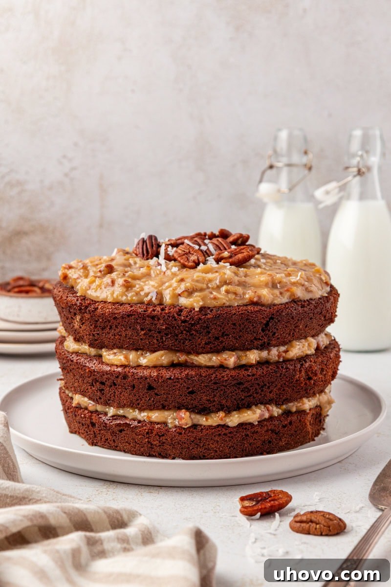 A beautifully assembled German chocolate cake on a white cake plate, showcasing its prominent layers and rich coconut-pecan frosting, bathed in natural light.