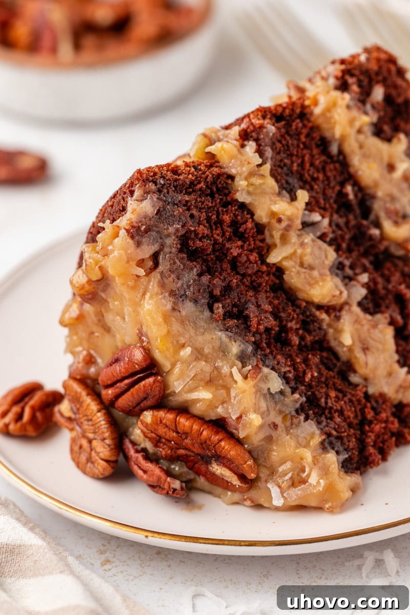 Close-up view of a perfectly sliced piece of German chocolate cake on a white plate, highlighting the moist chocolate layers and creamy, textured coconut-pecan frosting.