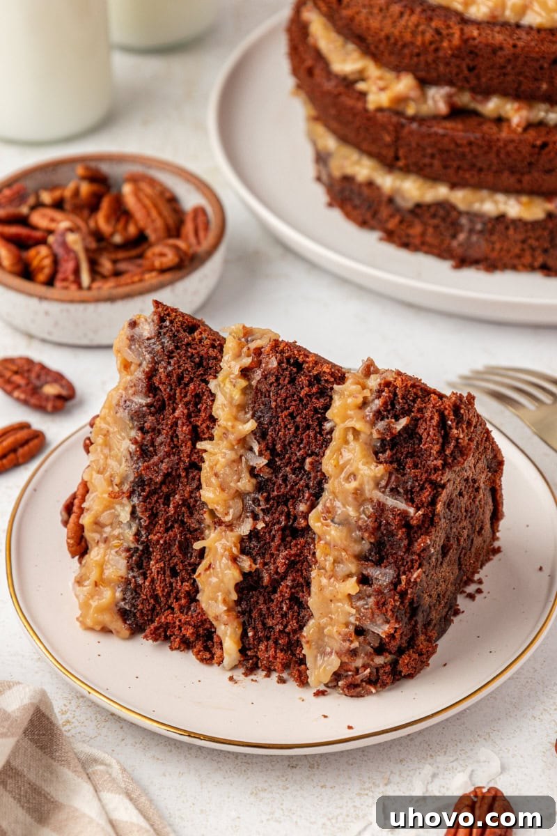 A large slice of German chocolate cake on a white plate in the foreground, with the remaining cake beautifully presented in the background, showing off the generous frosting.
