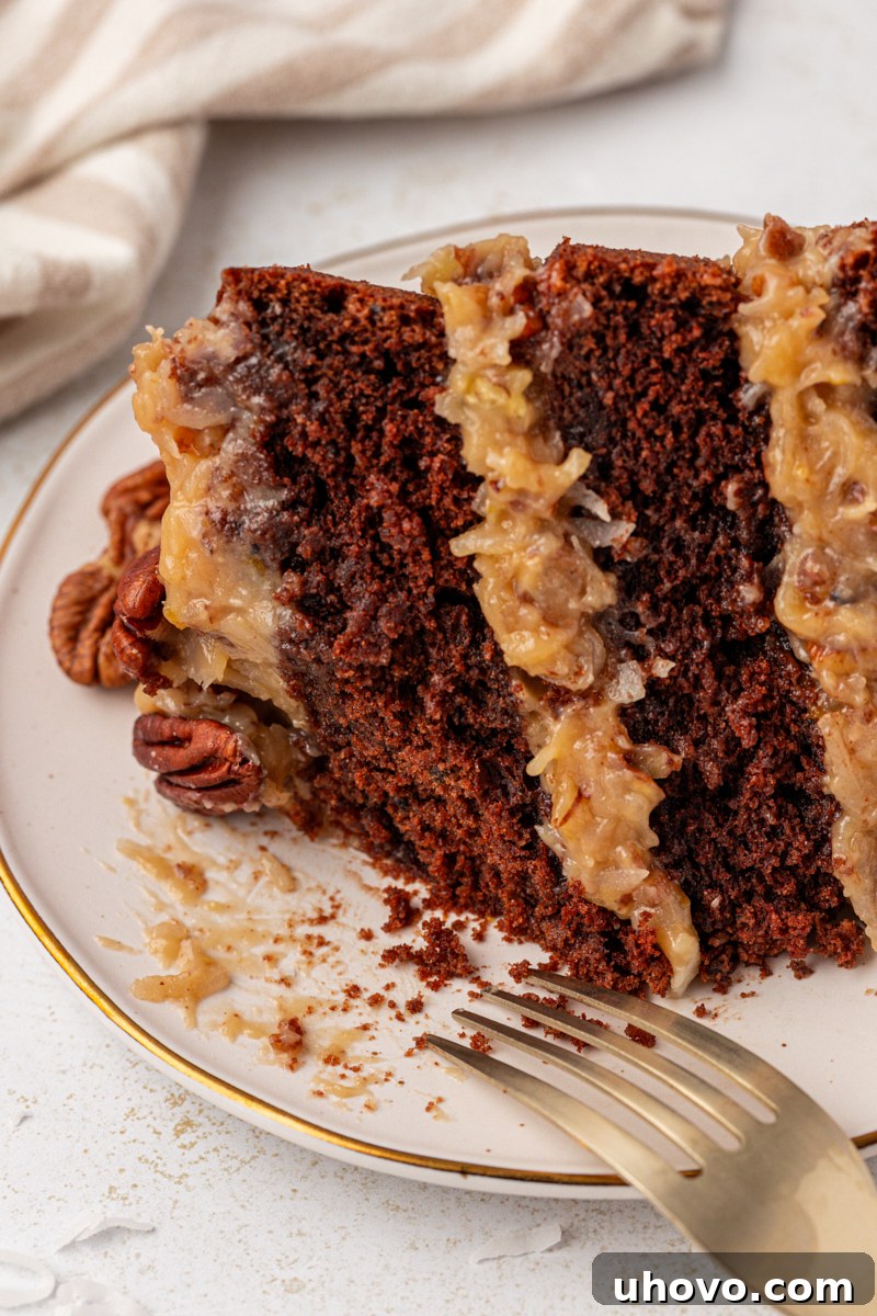A close-up of a slice of German chocolate cake on a white plate with a bite taken out, showing the moist interior, flaky coconut, and a fork resting beside it.