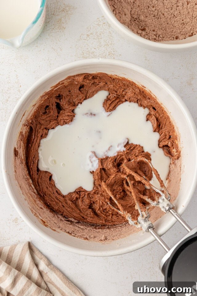 Overhead view showing buttermilk being smoothly incorporated into chocolate cake batter, alternating with dry ingredients to create a perfect texture.