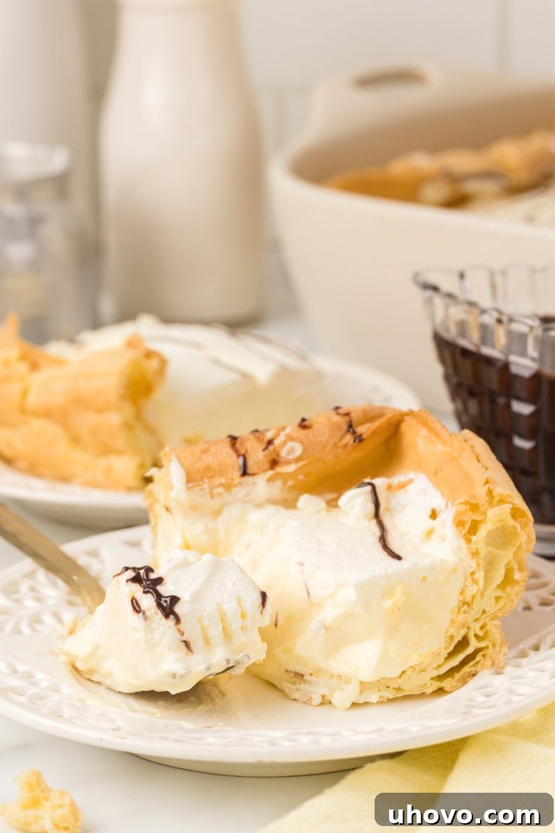 A beautifully presented slice of Cream Puff Cake on a white plate, with a fork taking a bite, showcasing the layered texture of choux pastry, vanilla cream, and whipped topping.