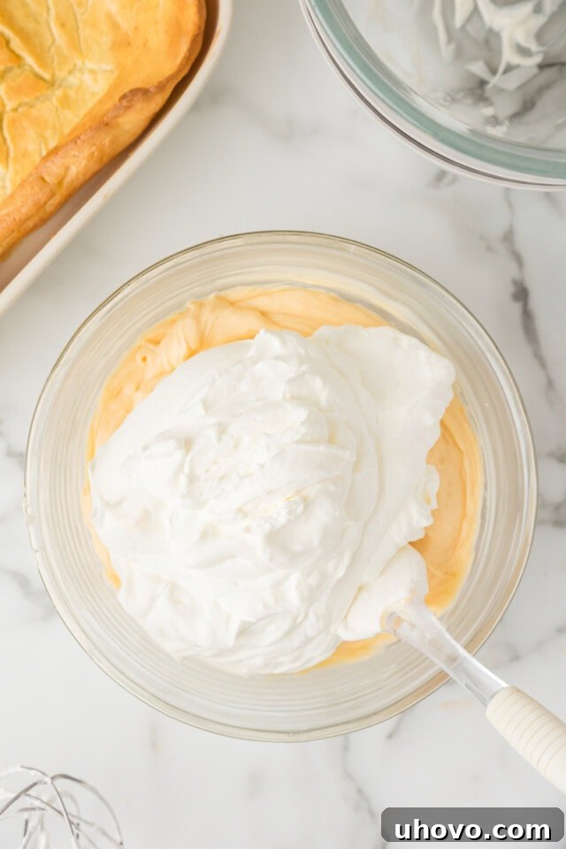 Overhead view of freshly whipped cream gently folded into the cream cheese and pudding mixture, creating the rich and airy cream puff cake filling.
