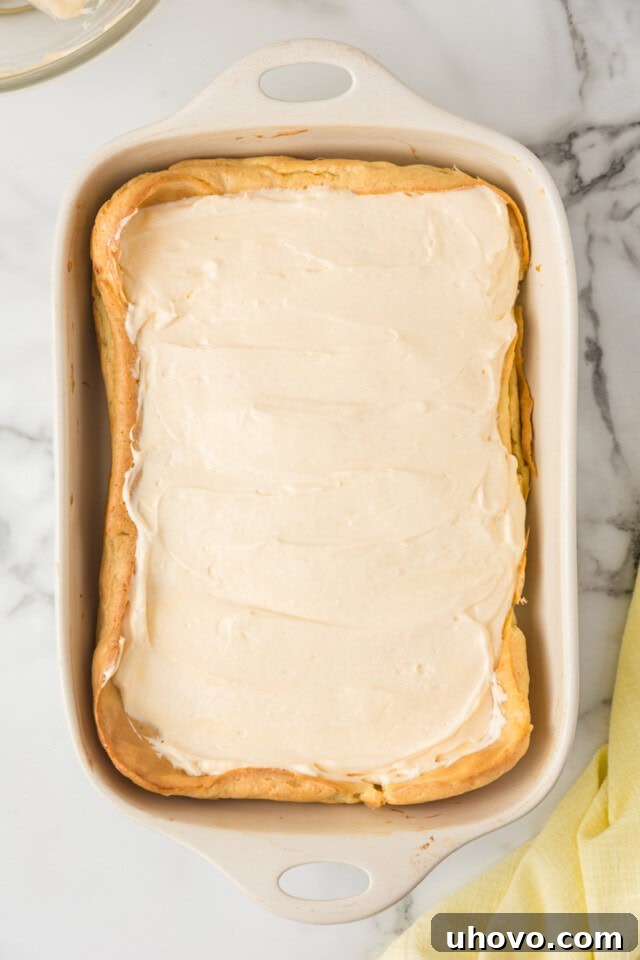 Overhead view of the creamy vanilla filling being spread smoothly and evenly over the cooled choux pastry crust in a white rectangular pan.