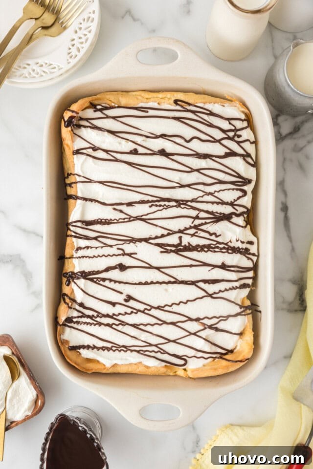 Overhead view of the finished Cream Puff Cake in a white rectangular pan, beautifully topped with whipped cream and a decorative drizzle of chocolate sauce.