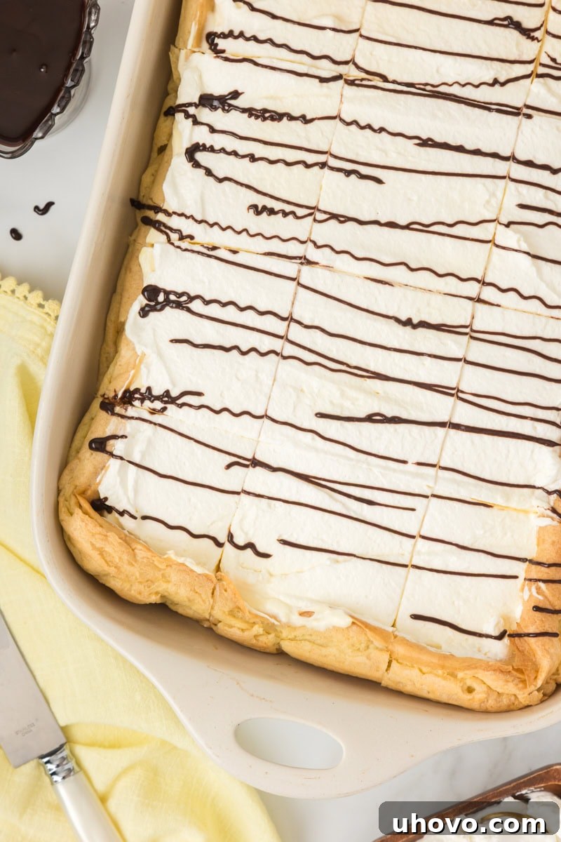 Overhead view of a Cream Puff Cake, freshly chilled and cut into neat squares, presented in a white rectangular baking pan, ready to be served.