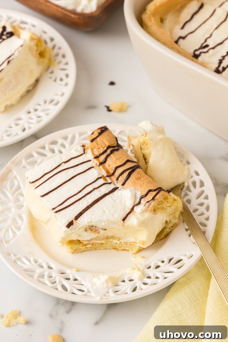 A delectable slice of Cream Puff Cake on a white plate, with a bite taken from a fork, emphasizing the cake's light, creamy layers. The remaining cake is softly blurred in the background.