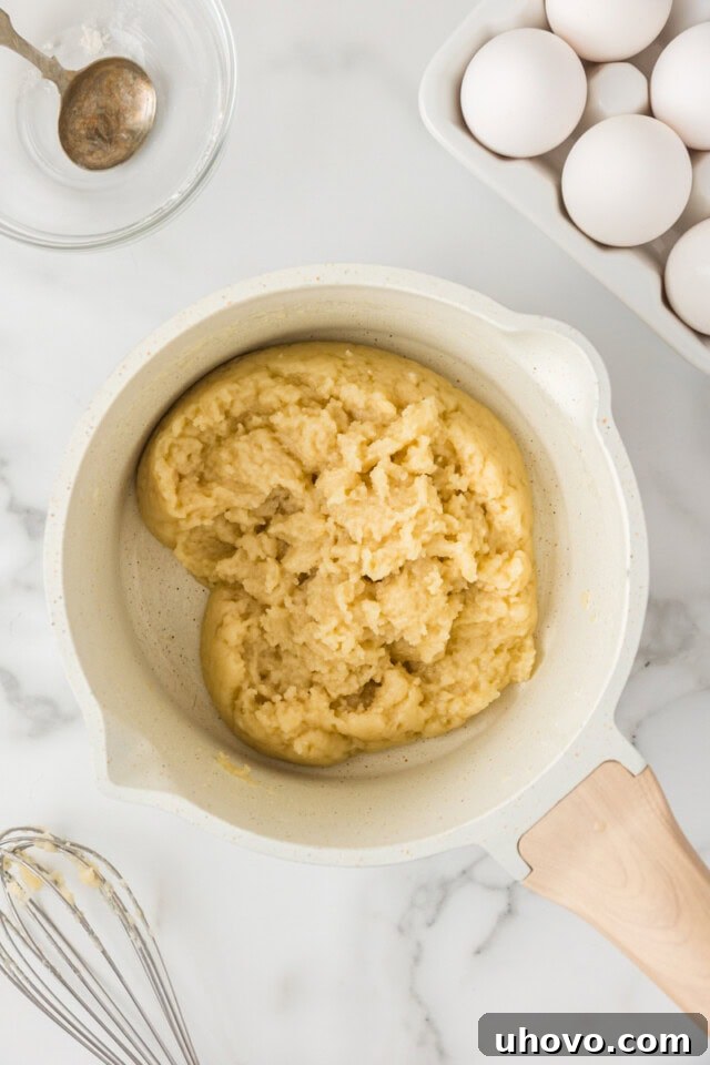 Overhead view of butter, water, and salt being heated in a saucepan, followed by the addition of flour, forming a dough for the choux pastry.