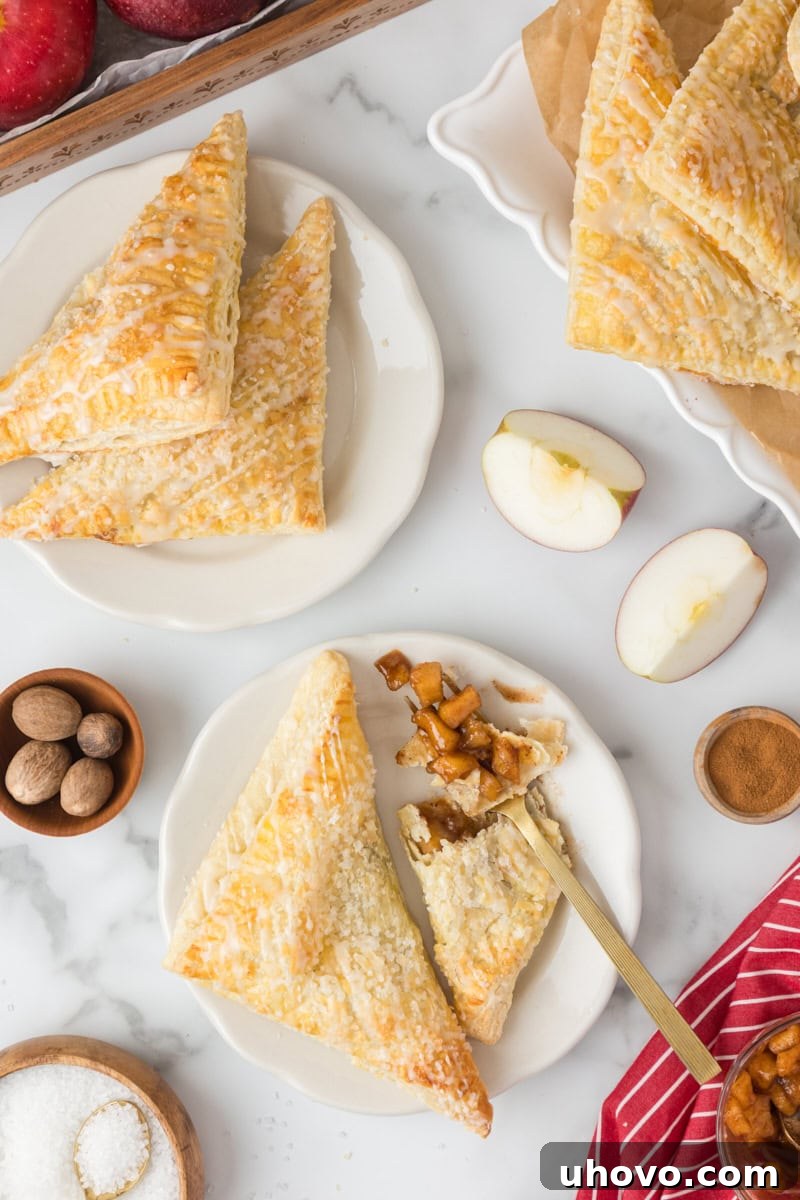 Overhead view of two baked and glazed apple turnovers artfully arranged on white plates, ready to be enjoyed.