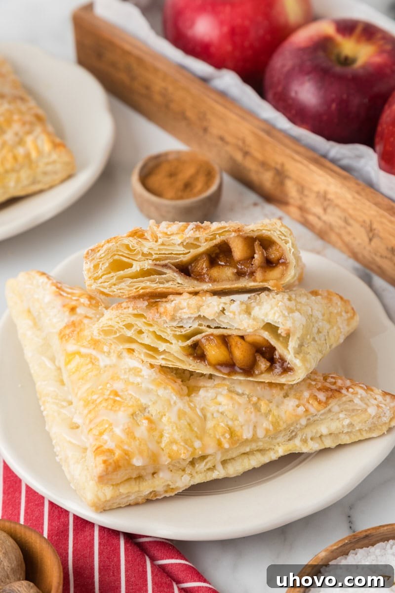 A delicious apple turnover cut in half, showcasing its tender apple filling and flaky layers, resting on top of another whole pastry.