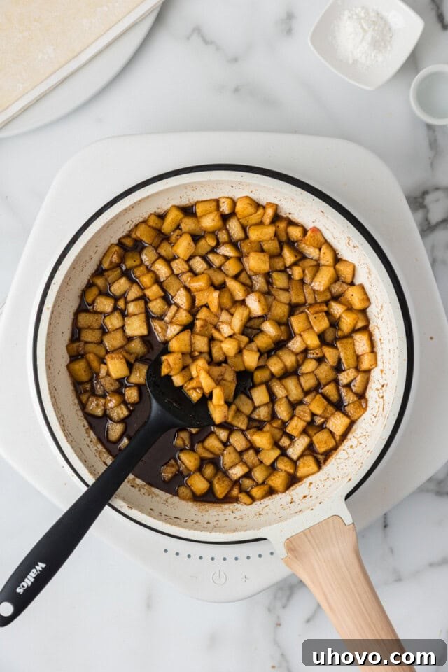Overhead view of cooked diced apples, sugars, spices, and lemon juice in a saucepan, now softened and thickened with cornstarch slurry.