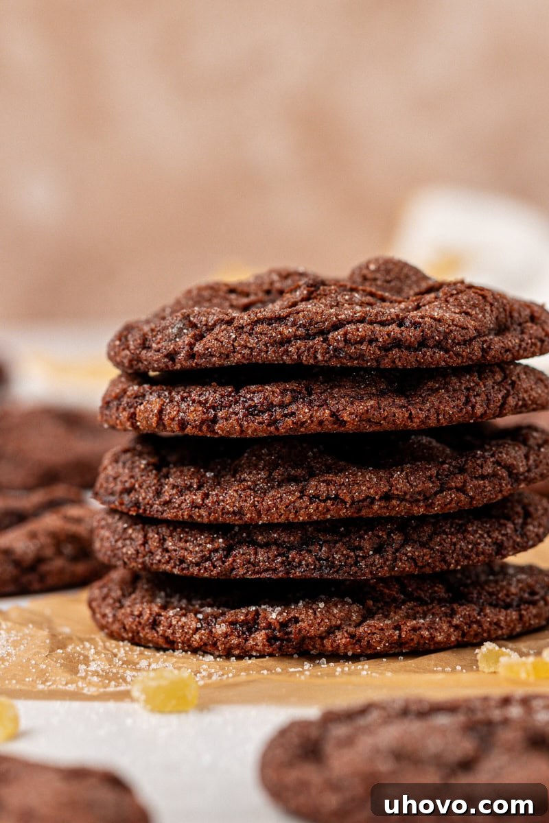 A perfectly arranged stack of six chocolate ginger cookies on parchment paper, highlighting their soft texture and sparkling sugar coating.