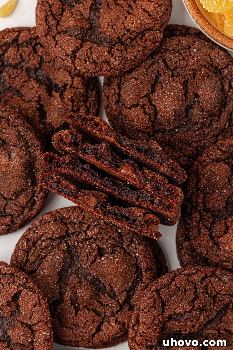An overhead view of two chocolate ginger cookies perfectly cut in half, revealing their soft interior, surrounded by more whole cookies on parchment paper.