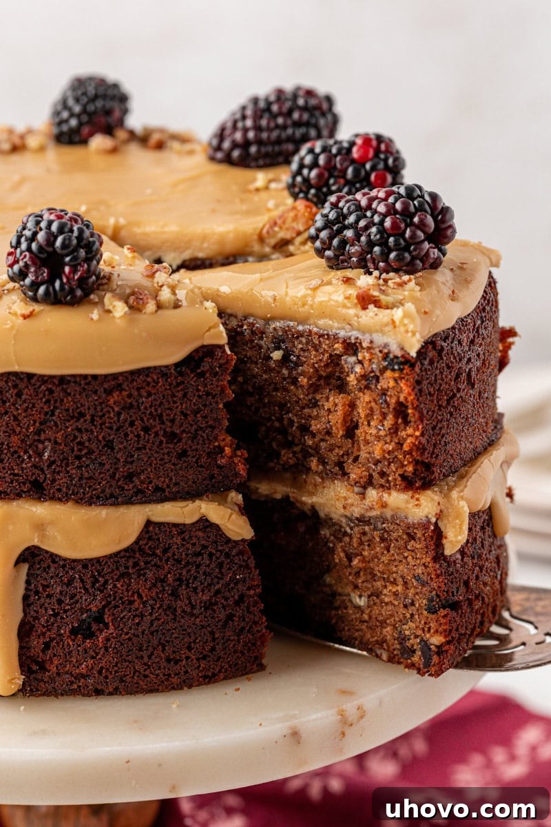 A sliced Kentucky Jam Cake showing its moist, spiced interior, with caramel frosting between the layers and on top, garnished with blackberries and chopped pecans. This cozy Southern jam cake is moist, spiced, and topped with creamy caramel frosting. A must-bake for winter!