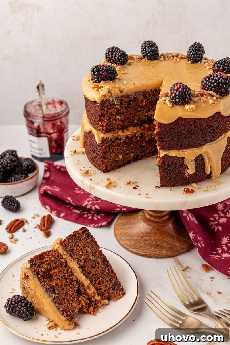 a slice of Kentucky jam cake on a white plate beside the remaining cake on a marble cake stand. This cozy Southern jam cake is moist, spiced, and topped with creamy caramel frosting. A must-bake for winter!