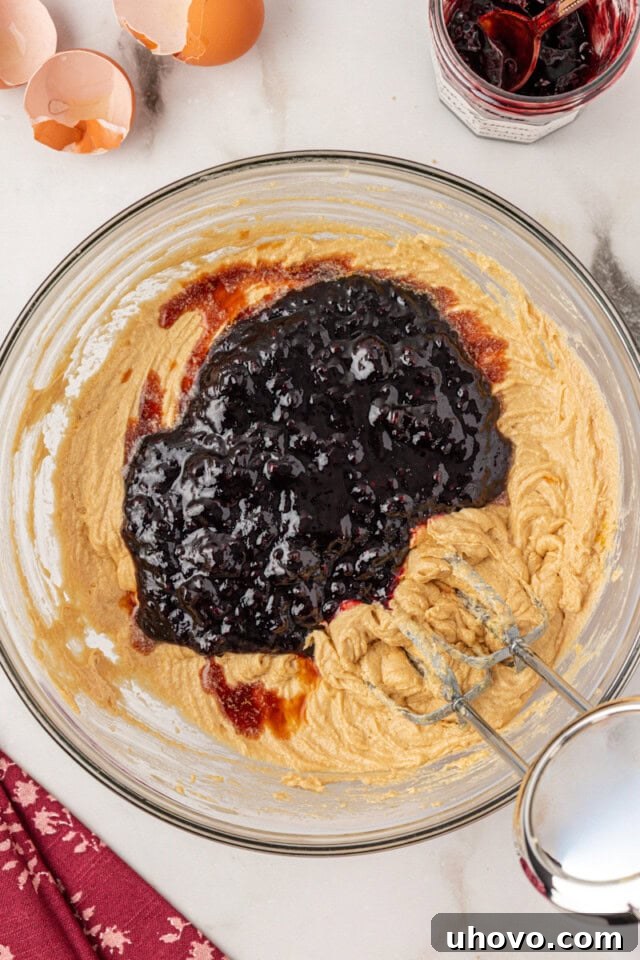 overhead view of blackberry jam and vanilla extract added to partially mixed cake batter