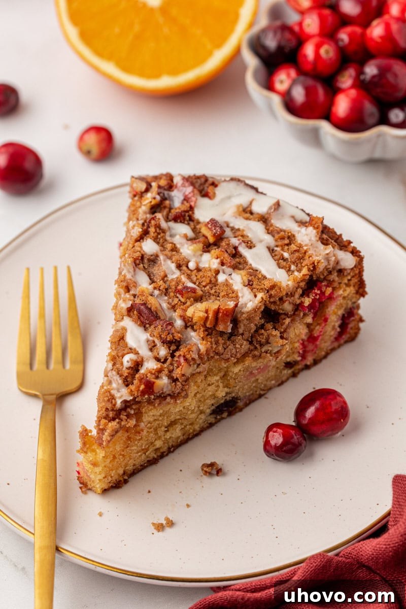 A beautifully sliced cranberry coffee cake topped with an orange glaze, served on a pristine white plate, ready for a festive holiday brunch or a cozy winter morning treat.