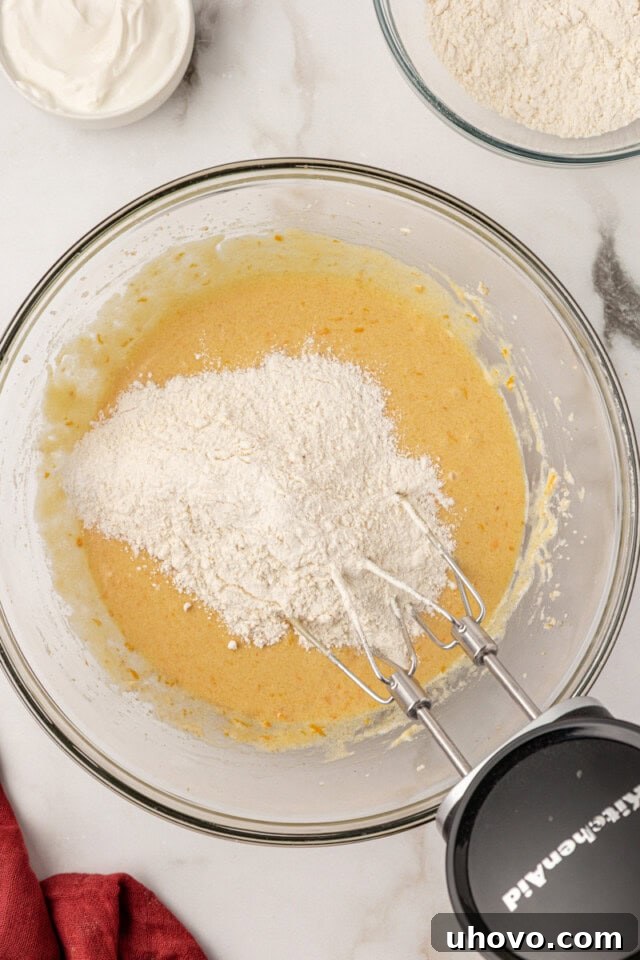 Overhead view of a portion of the dry flour mixture being added to the wet cake batter in a large mixing bowl.