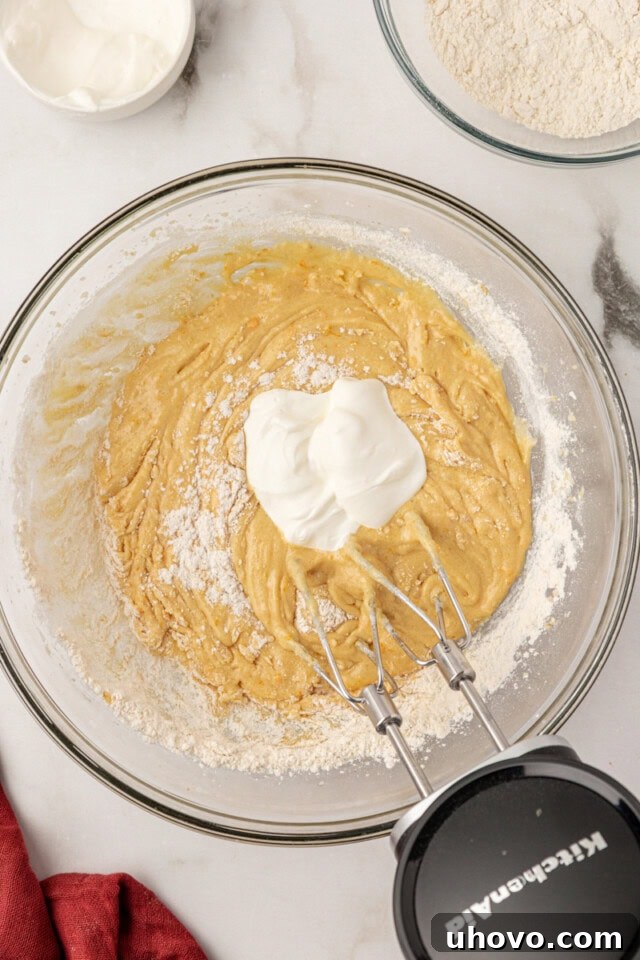 Overhead view of a portion of sour cream being added to the cake batter, alternating with the dry ingredients.